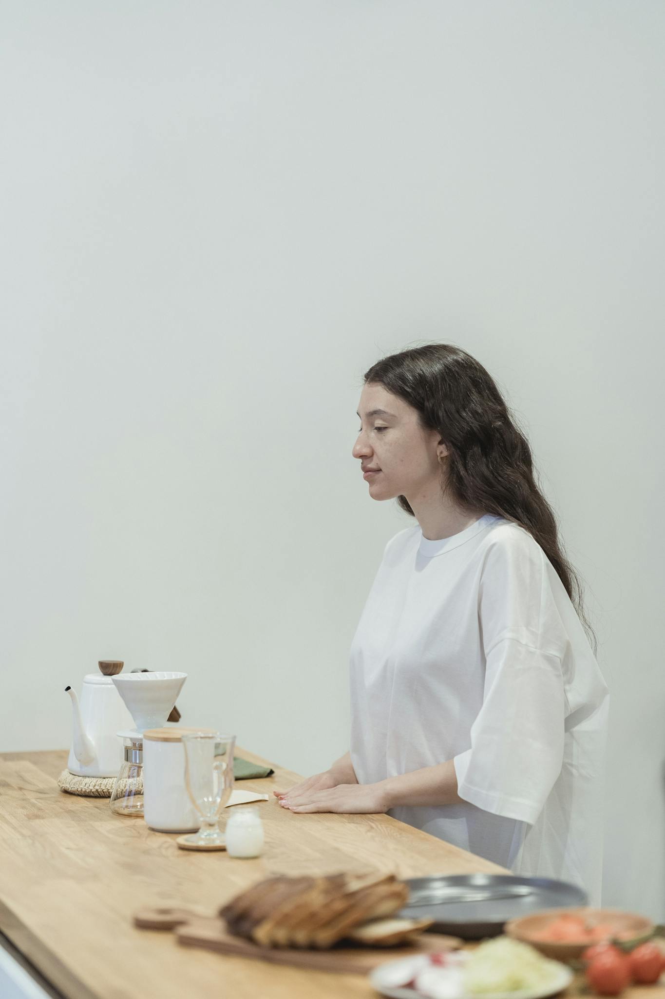 A woman stands by a coffee counter with drinks in a minimalist cafe setting.